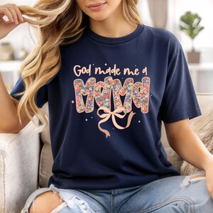 Pu&ograve; includere: T-shirt blu navy con la scritta "God made me a Mama". La parola "Mama" &egrave; riempita con un motivo floreale. Un fiocco rosa chiaro &egrave; sotto il testo, con piccoli accenti di stelle.