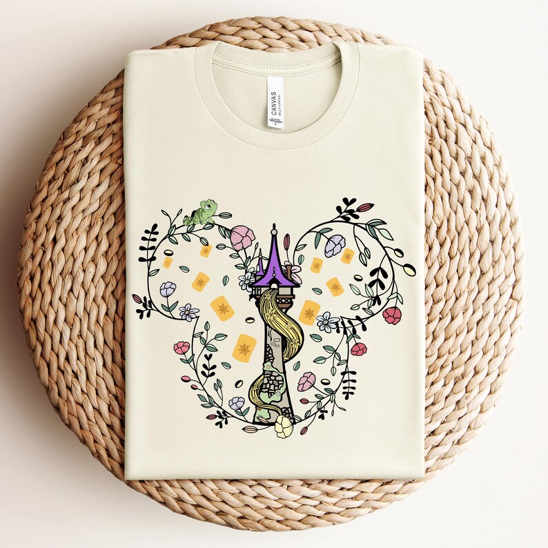 May include: A cream-colored t-shirt with a graphic of a purple and yellow tower with a green vine and flowers in the shape of Mickey Mouse ears.