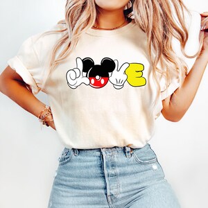May include: A white t-shirt with a graphic of Mickey Mouse's hands forming the word "LOVE".