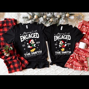 Puede incluir: Dos camisetas negras con un dise&ntilde;o de Mickey Mouse navide&ntilde;o. Las camisetas dicen "Merry & Engaged" con el a&ntilde;o 2024 y "The Smith" con "First Christmas Mr. and Mrs."