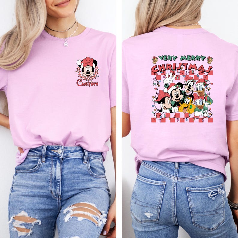 May include: A light pink t-shirt featuring a Minnie Mouse graphic with the word "Custom" on the front. The back of the shirt displays a "Very Merry Christmas" design with Mickey Mouse, Goofy, Donald Duck, and Pluto.