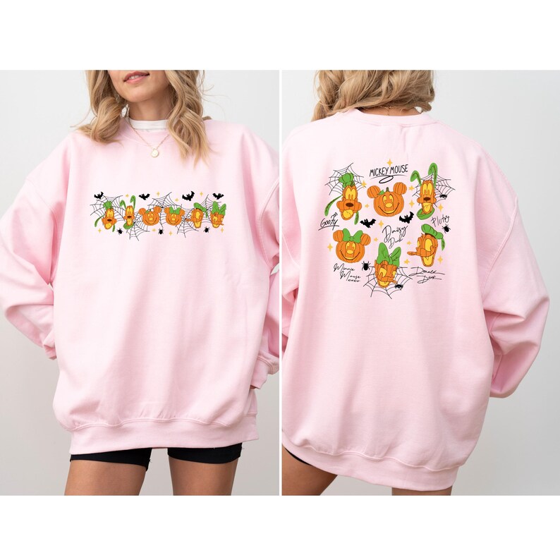 May include: A light pink sweatshirt featuring Halloween-themed character designs. The front displays a row of cartoon pumpkins with character faces, spiderwebs, and bats. The back has character pumpkin designs with the words "Mickey Mouse".