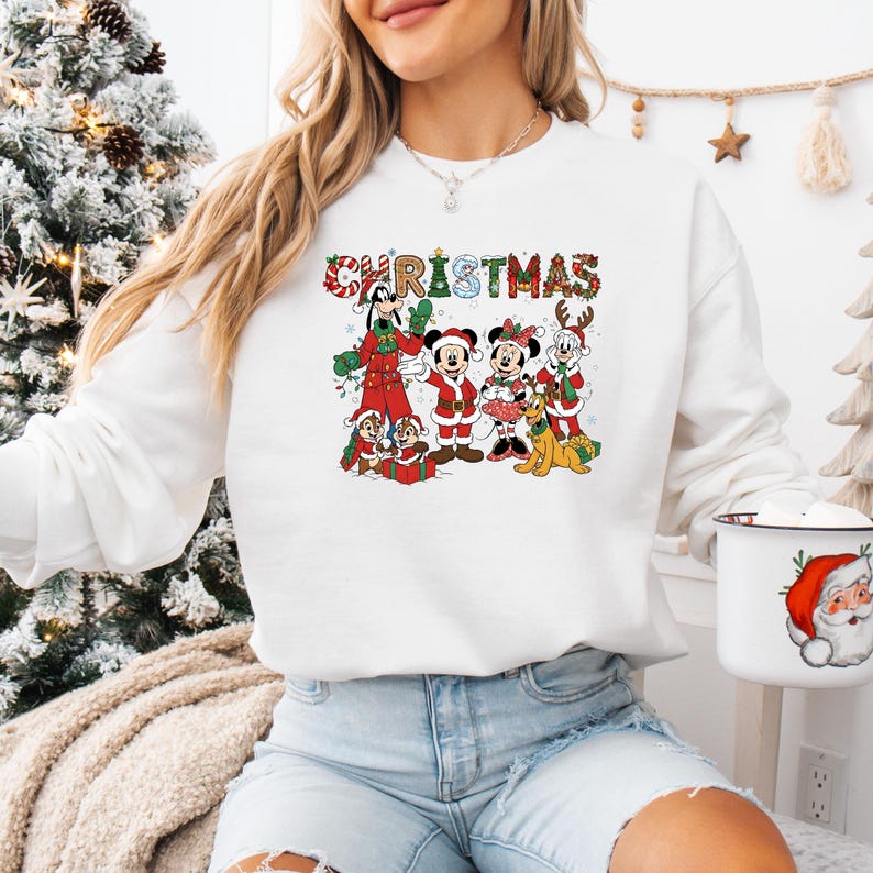 May include: White sweatshirt featuring a colorful Christmas graphic with Disney characters. The word "CHRISTMAS" is displayed above the characters. The graphic includes Mickey Mouse, Minnie Mouse, Goofy, Donald Duck, Chip and Dale, and Pluto in festive attire.