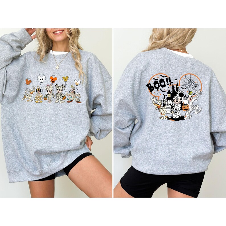 K&ouml;nnte beinhalten: Ein meliertes graues Sweatshirt mit einem Halloween-Motiv. Auf der Vorderseite sind Cartoon-Figuren als Mumien verkleidet, die Luftballons halten. Auf der R&uuml;ckseite sind ein Schloss, ein Spinnennetz und das Wort "BOO!!" mit weiteren Figuren abgebildet.