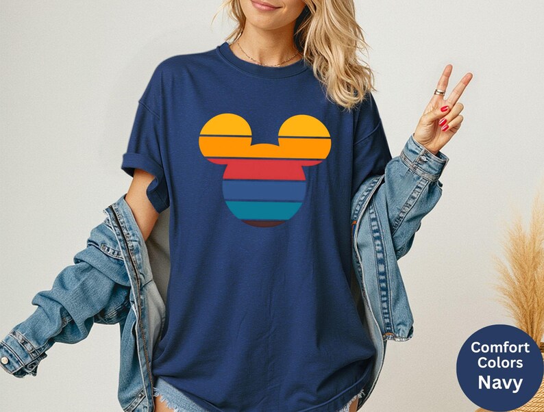 K&ouml;nnte beinhalten: Marineblaues T-Shirt mit einem Retro-Mickey-Mouse-Silhouette-Design in Sonnenuntergangsfarben. Die Grafik enth&auml;lt horizontale Streifen in Orange, Gelb, Rot und Blau. Das Shirt ist im Comfort Colors-Stil.