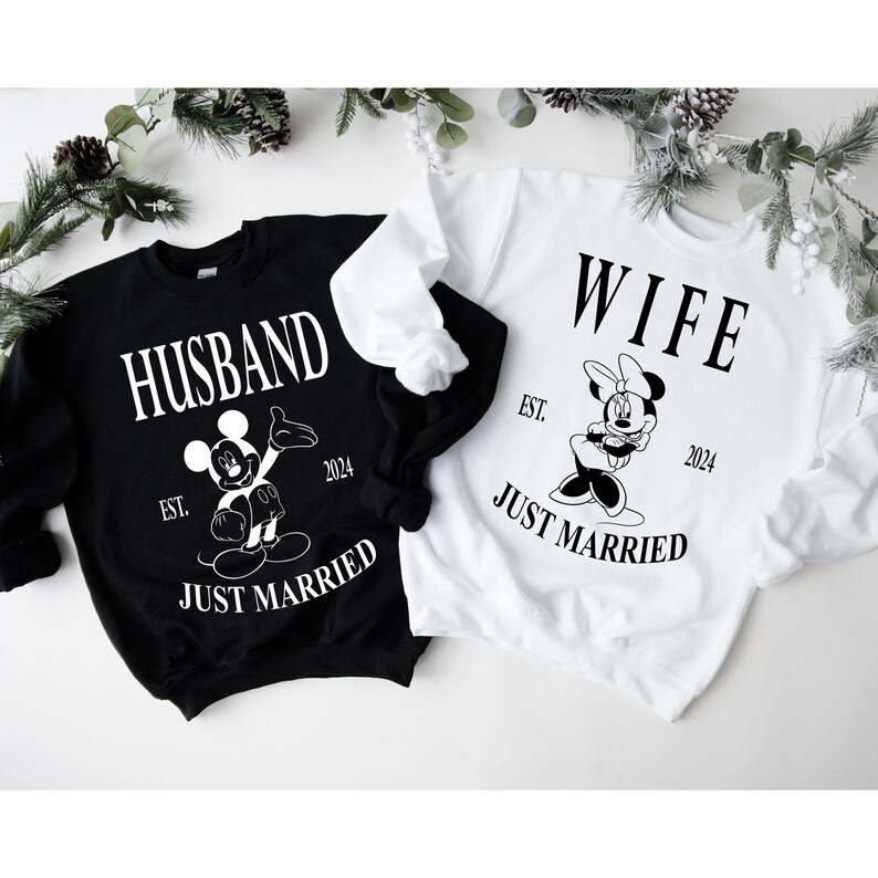 May include: Black and white sweatshirt with the text "Husband" and a Mickey Mouse illustration. White text reads "Est. 2024 Just Married".  White sweatshirt with the text "Wife" and a Minnie Mouse illustration. White text reads "Est. 2024 Just Married".