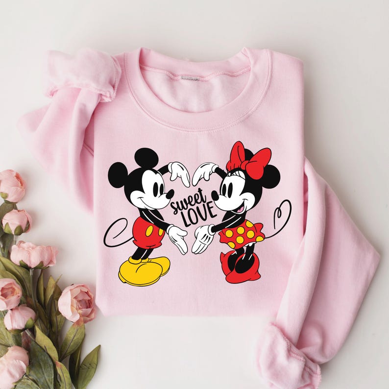 Może przedstawiać: R&oacute;żowa bluza z nadrukiem przedstawiającym Myszki Miki i Minnie trzymające się za ręce w kształcie serca. Na bluzie widnieje napis "sweet love".
