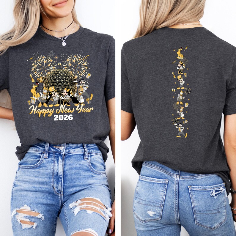 May include: Dark gray t-shirt with a festive "Happy New Year 2026" design featuring fireworks and cartoon characters. The back of the shirt has a vertical design of the same characters. The shirt is paired with blue jeans.