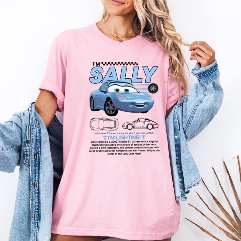May include: A light pink t-shirt featuring a blue cartoon car with the text "I'M SALLY". Below the car are two line drawings of the car. The text "I'M LIGHTING!" is also on the shirt. The shirt also has text describing the car.