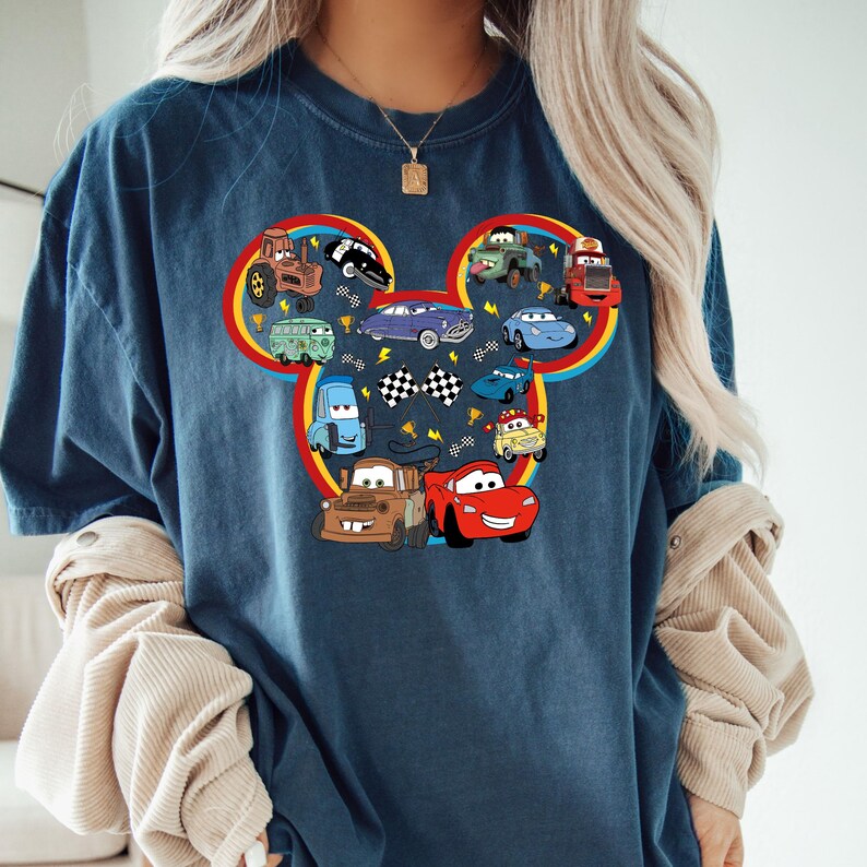 May include: A blue t-shirt with a cartoon image of a Mickey Mouse head made up of various cars from the Disney Pixar movie Cars. The cars are in various colors, including red, yellow, blue, and green.