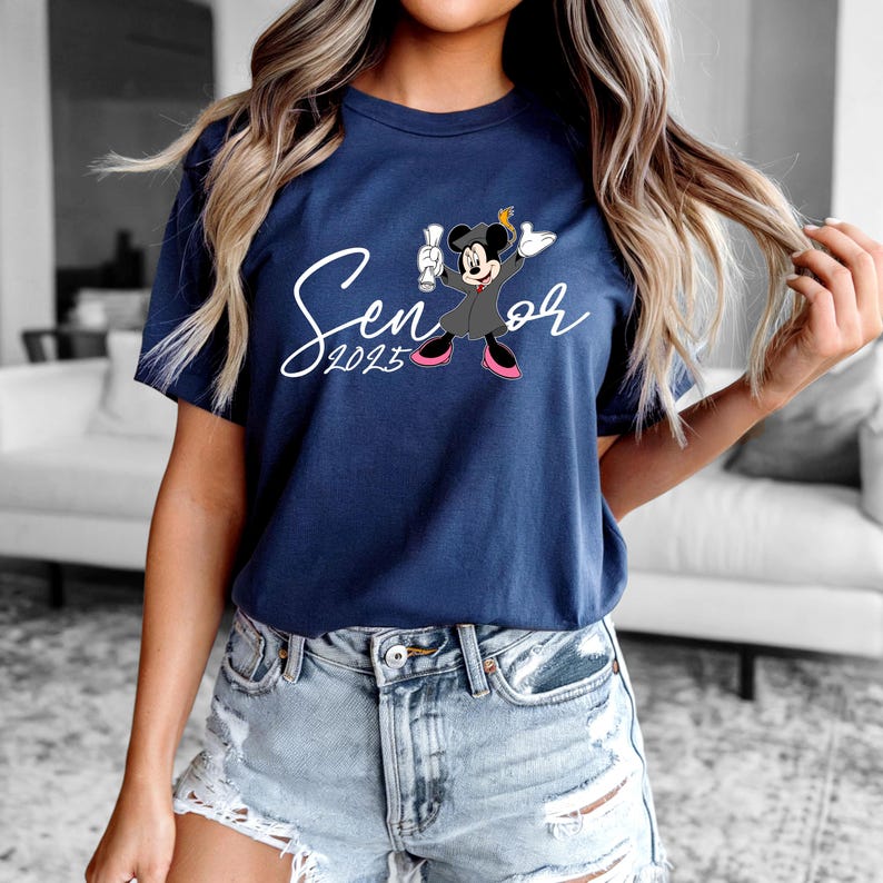 May include: A navy blue t-shirt featuring a white graphic of Mickey Mouse wearing a graduation cap and gown. The text "Senior 2023" is written in white cursive script.