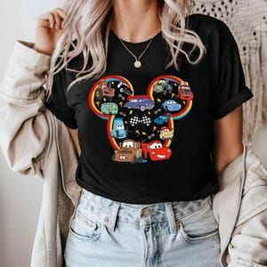 May include: Black t-shirt with a Mickey Mouse silhouette design featuring various Cars characters, including Lightning McQueen, Mater, and other vehicles. The design is in a colorful cartoon style.