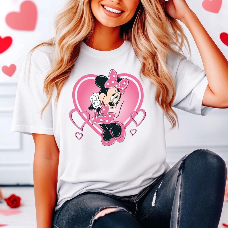 May include: White t-shirt with a pink heart design featuring Minnie Mouse in a pink polka dot dress. The heart is surrounded by smaller pink hearts.