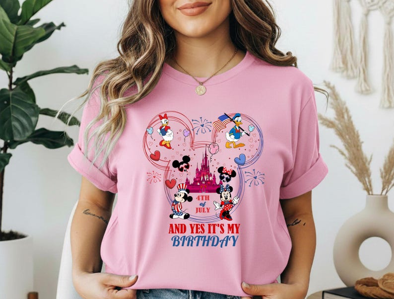 May include: Pink t-shirt featuring a Mickey Mouse design with Daisy Duck, Donald Duck, Mickey Mouse, and Minnie Mouse. The design includes a castle, hearts, fireworks, and the text "4th of July AND YES IT'S MY BIRTHDAY."