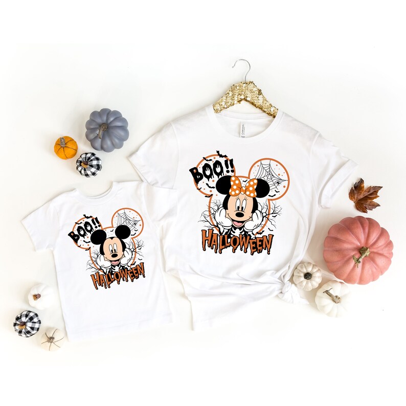 Puede incluir: Dos camisetas blancas con un dise&ntilde;o de Halloween de Mickey Mouse. El dise&ntilde;o presenta a Mickey Mouse con una telara&ntilde;a y las palabras "Boo!" y "Halloween".