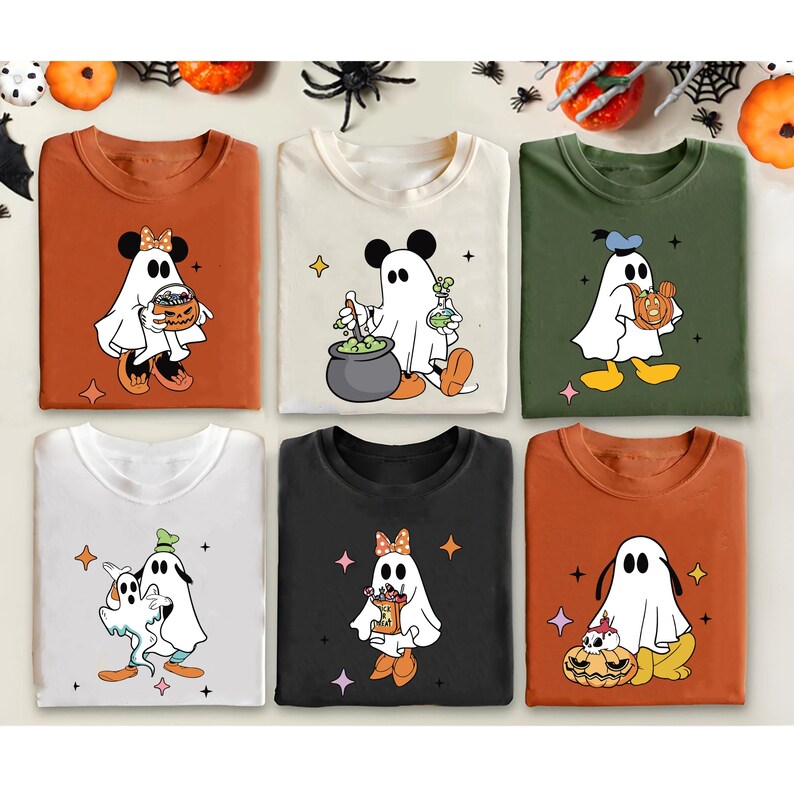 May include: Six long-sleeved t-shirts in various colors, each featuring a cartoon ghost character with Mickey Mouse ears. The ghosts are holding pumpkins, cauldrons, and potion bottles. Halloween-themed apparel.