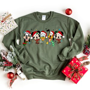 May include: Green Christmas sweatshirt featuring Mickey Mouse, Donald Duck, Goofy, and Pluto wearing Santa hats and scarves.