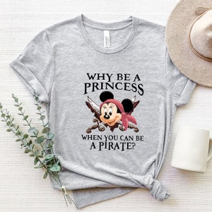 May include: Gray t-shirt with a black and white graphic of Mickey Mouse dressed as a pirate. The text on the shirt reads "Why be a princess when you can be a pirate?"