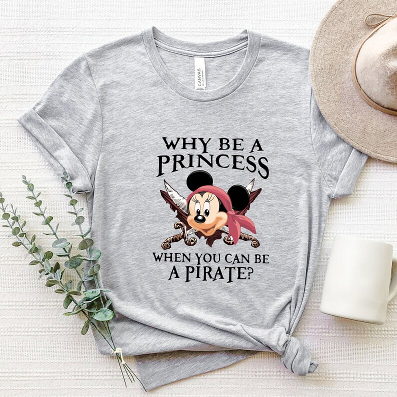May include: Gray t-shirt with a black and white graphic of Mickey Mouse dressed as a pirate. The text on the shirt reads "Why be a princess when you can be a pirate?"