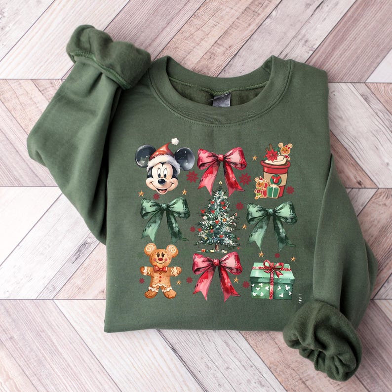 May include: A green sweatshirt with a Christmas theme featuring Mickey Mouse, a Christmas tree, presents, and gingerbread men. The sweatshirt has a crew neck and long sleeves.