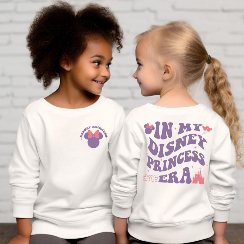 Puede incluir: Dos chicas vistiendo camisas blancas de manga larga con un dise&ntilde;o de princesa Disney morado y rosa. Una camisa tiene una cabeza de Mickey Mouse morada con un lazo rosa en la parte delantera. La otra camisa tiene el texto "In My Disney Princess Era" en la parte posterior con un lazo rosa, un castillo morado y flores rosas.