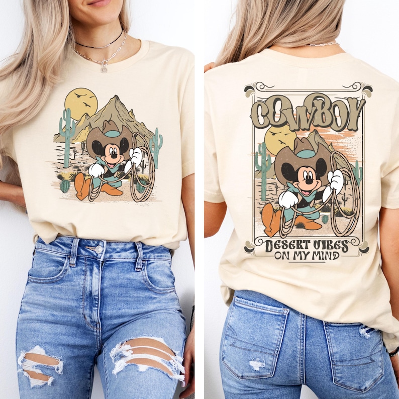 May include: A beige t-shirt with a cartoon image of Mickey Mouse dressed as a cowboy. The front of the shirt features Mickey Mouse holding a lasso. The back of the shirt features a graphic with the text "COWBOY" and "DESERT VIBES ON MY MIND".