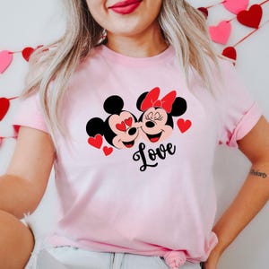 May include: Pink t-shirt with a graphic of Mickey Mouse and Minnie Mouse with hearts and the word "Love" printed on the front.