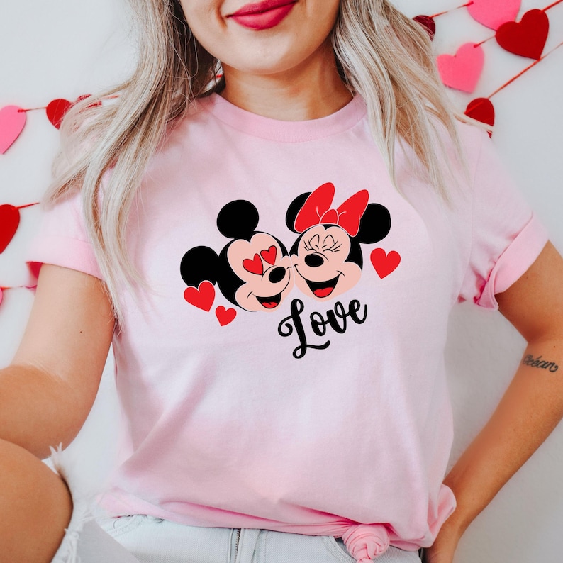 May include: Pink t-shirt with a graphic of Mickey Mouse and Minnie Mouse with hearts and the word "Love" printed on the front.