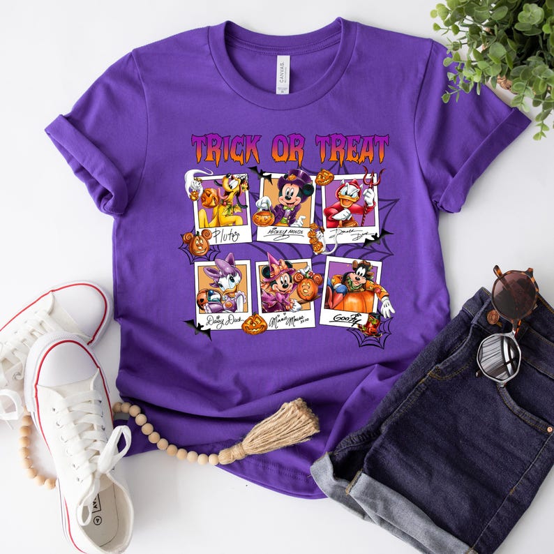 May include: Purple t-shirt with the text "Trick or Treat" in orange and black. The shirt features six cartoon character portraits in Halloween costumes, including Pluto, Mickey Mouse, Donald Duck, Daisy Duck, Minnie Mouse, and Goofy.