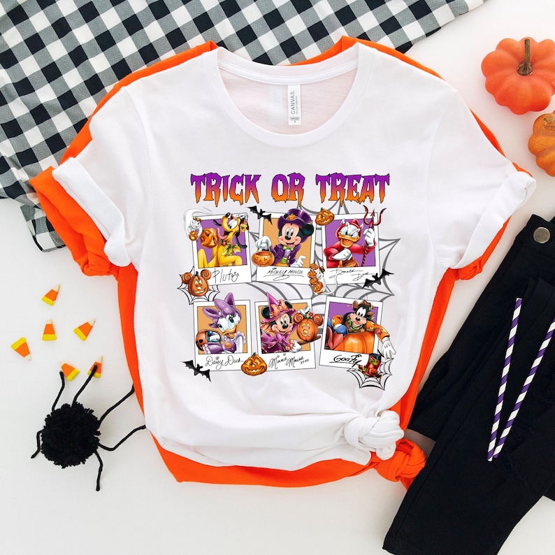 May include: White t-shirt with a Halloween-themed graphic featuring Disney characters. The design includes the text "Trick or Treat" in purple, along with images of Pluto, Mickey Mouse, Donald Duck, Daisy Duck, Minnie Mouse, and Goofy in Halloween costumes.