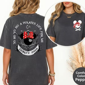 May include: Dark grey t-shirt with a pirate-themed design. The back features an anchor with Minnie Mouse ears and a red bow, the text "YO HO HO A PIRATES LIFE FOR ME" and "DISNEY 2026". The front has a pirate Mickey Mouse head.