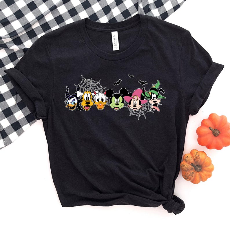 Pu&ograve; includere: Maglietta nera con una grafica di Topolino, Paperino, Pippo, Pluto e Minnie Mouse vestiti con costumi di Halloween. I personaggi sono circondati da ragnatele e pipistrelli.