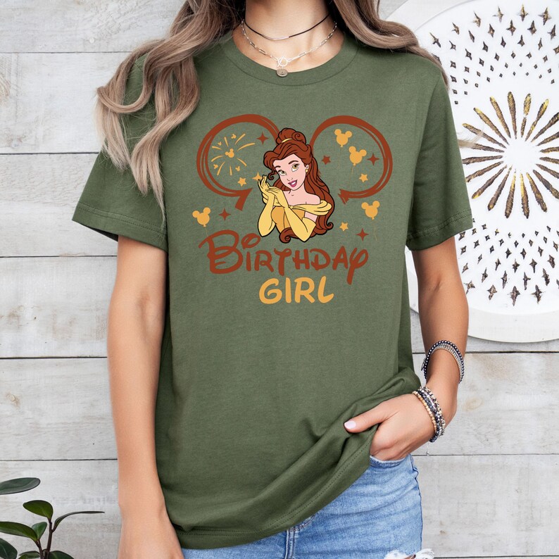 May include: Green t-shirt with a graphic of Belle from Beauty and the Beast wearing a yellow dress and a crown. The graphic is surrounded by Mickey Mouse ears and the text "Be Birthday Girl".