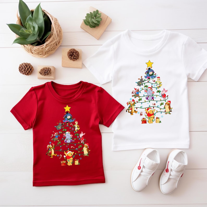 Pu&ograve; includere: Due magliette per bambini, una rossa e una bianca, ciascuna con un disegno di albero di Natale fatto di personaggi dei cartoni animati. L'albero &egrave; sormontato da una stella gialla e decorato con luci a stringa. Scarpe da ginnastica bianche sotto.