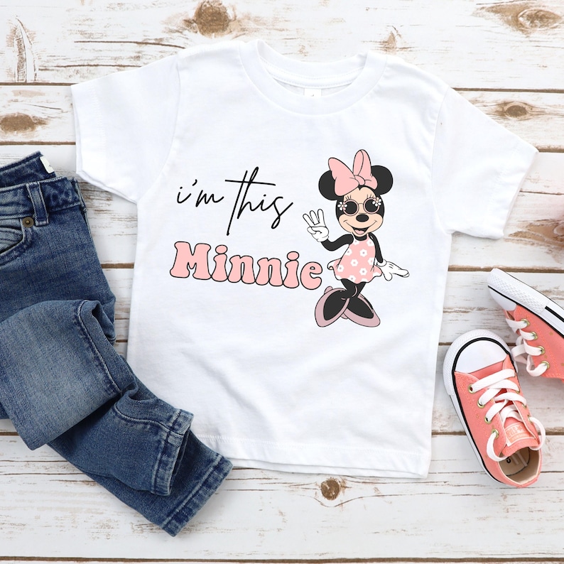Puede incluir: Camiseta blanca con un gr&aacute;fico rosa de Minnie Mouse y el texto "i'm this Minnie".