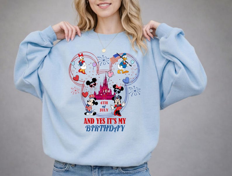 May include: Light blue sweatshirt featuring a Mickey Mouse-shaped design with patriotic characters like Mickey, Minnie, Donald, and Daisy Duck. The design includes fireworks, hearts, and the text "4th of July" and "And Yes It's My Birthday."