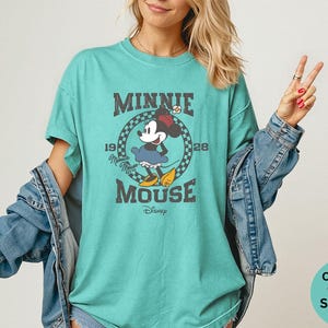 May include: Seafoam green t-shirt featuring a vintage graphic of Minnie Mouse. The design includes the text "MINNIE MOUSE" and the year "1928". The shirt is a Comfort Colors brand. The shirt is a relaxed fit.