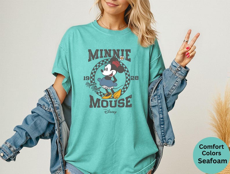 May include: Seafoam green t-shirt featuring a vintage graphic of Minnie Mouse. The design includes the text "MINNIE MOUSE" and the year "1928". The shirt is a Comfort Colors brand. The shirt is a relaxed fit.