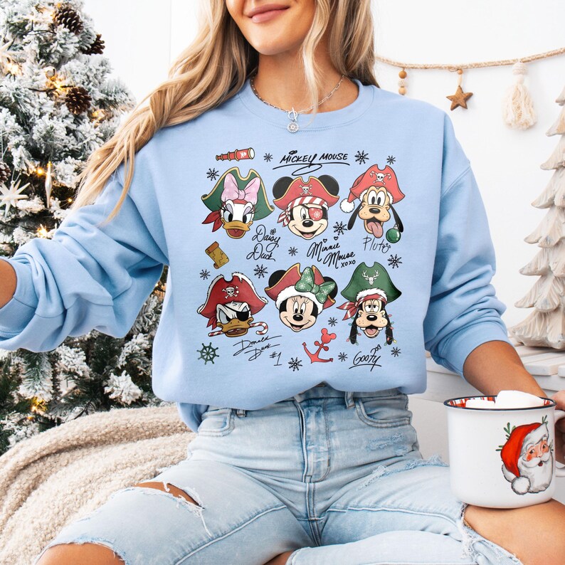 May include: Light blue sweatshirt featuring cartoon pirate versions of Mickey Mouse, Minnie Mouse, Donald Duck, Daisy Duck, and Goofy. The sweatshirt has the words "Mickey Mouse" and character names. The design includes pirate hats and nautical elements.