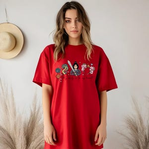 May include: A red t-shirt with a graphic design featuring a warrior woman, a dragon, flowers, and the text "My duty is to my heart!". The design incorporates blue, pink, and gold. The shirt has a relaxed, oversized fit.