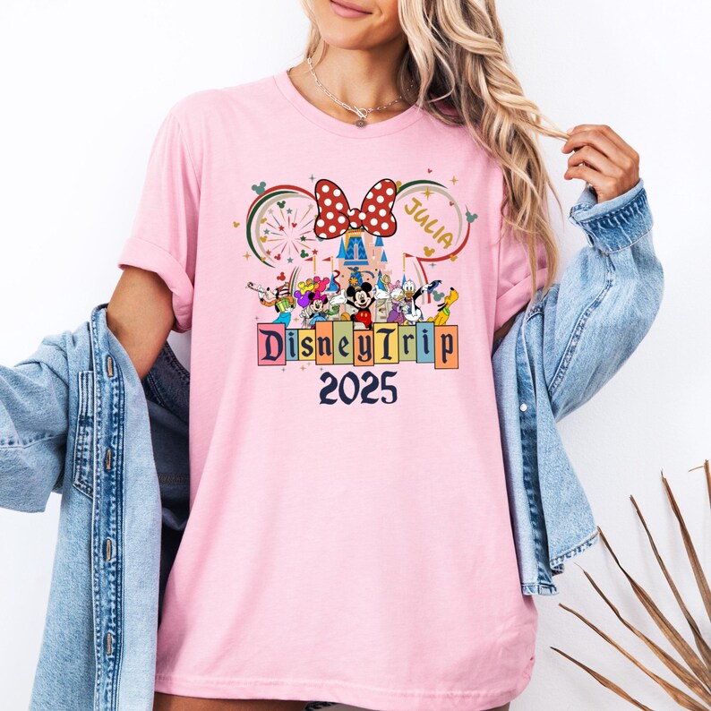 May include: Pink t-shirt with a graphic of Mickey Mouse and friends in front of Cinderella's Castle. The text "Disney Trip 2025" is below the graphic. The text "Julia" is on the right side of the graphic.