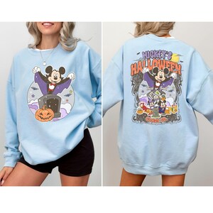 May include: Light blue sweatshirt with a Mickey Mouse Halloween graphic on the front and a Mickey Mouse Halloween Candy Co. graphic on the back.