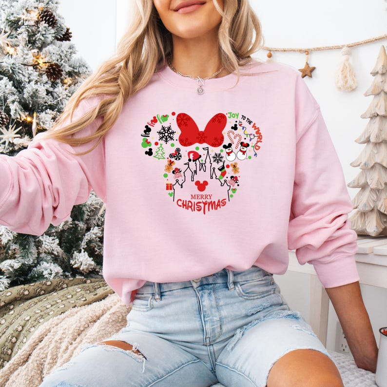 Pu&ograve; includere: Una felpa rosa chiaro con un design festivo di Minnie Mouse. Il design include un fiocco rosso, icone natalizie e la scritta "Merry Christmas". La felpa &egrave; a maniche lunghe e girocollo.