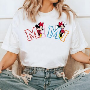 May include: White t-shirt with a graphic of Mickey Mouse characters spelling out "MIMI" in colorful letters.