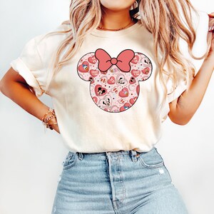 May include: A white t-shirt with a pink and red Minnie Mouse head graphic. The graphic features a pink bow and hearts with the text "Crazy in Love" on some of the hearts.