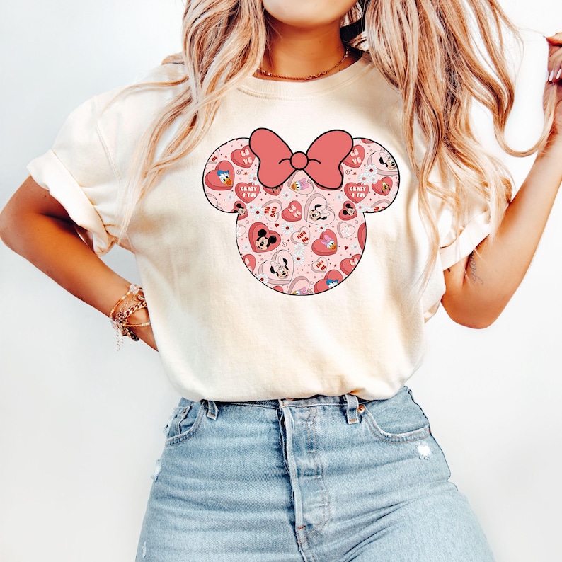 May include: A white t-shirt with a pink and red Minnie Mouse head graphic. The graphic features a pink bow and hearts with the text "Crazy in Love" on some of the hearts.