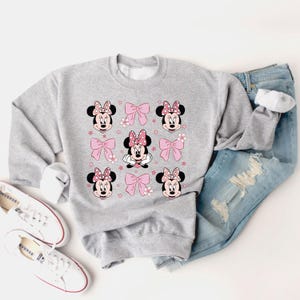 May include: A gray sweatshirt with a print of Minnie Mouse wearing a pink bow and surrounded by pink bows and stars.