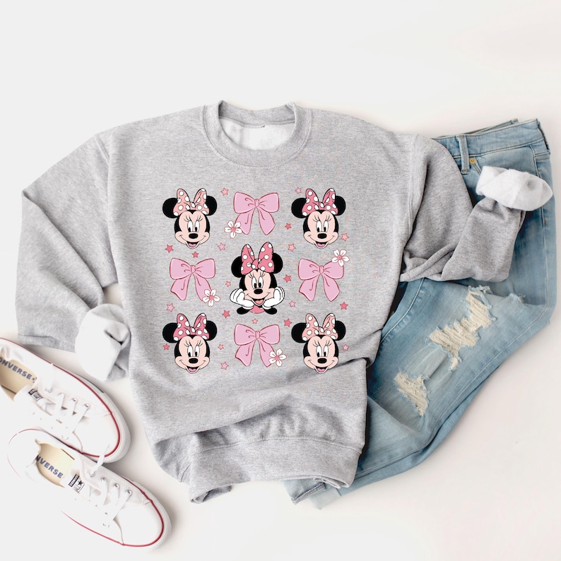 May include: A gray sweatshirt with a print of Minnie Mouse wearing a pink bow and surrounded by pink bows and stars.