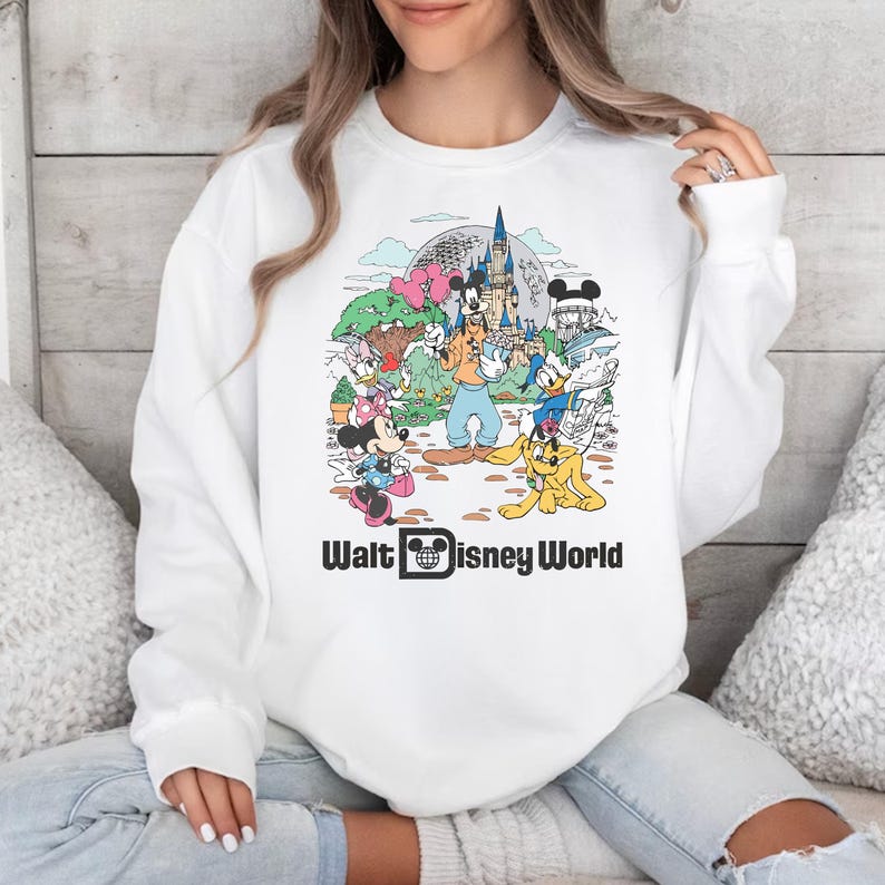 May include: White sweatshirt with a colorful graphic print of Mickey Mouse and other Disney characters in front of Cinderella's Castle. The text "Walt Disney World" is printed below the graphic.