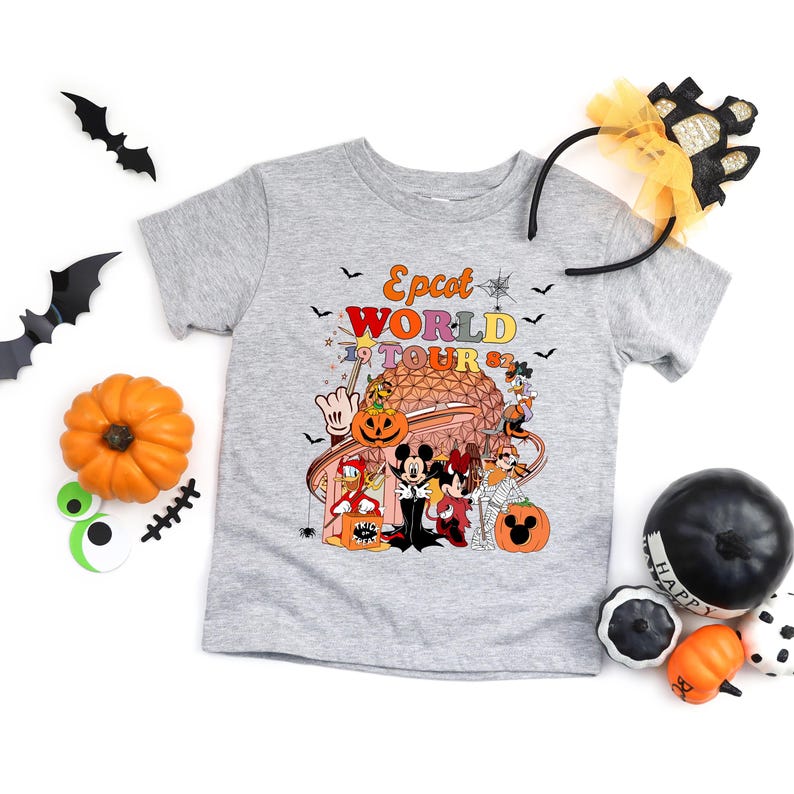May include: A gray t-shirt with a colorful graphic featuring Disney characters in Halloween costumes in front of a stylized building. The text "Epcot World Tour 82" is above the graphic. Halloween decorations surround the shirt.